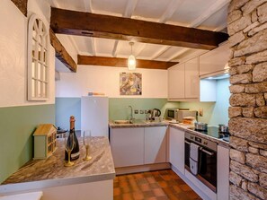 Cocina compacta con pared de piedra, techo de madera y una pequeña isla con fregadero.