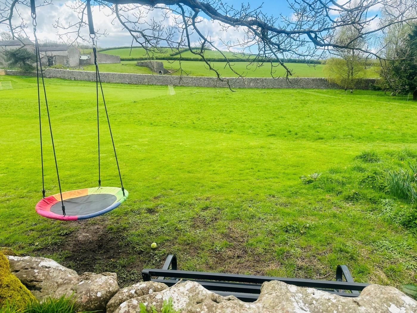 Un champ herbeux avec une balançoire et un mur de pierre en arrière-plan.