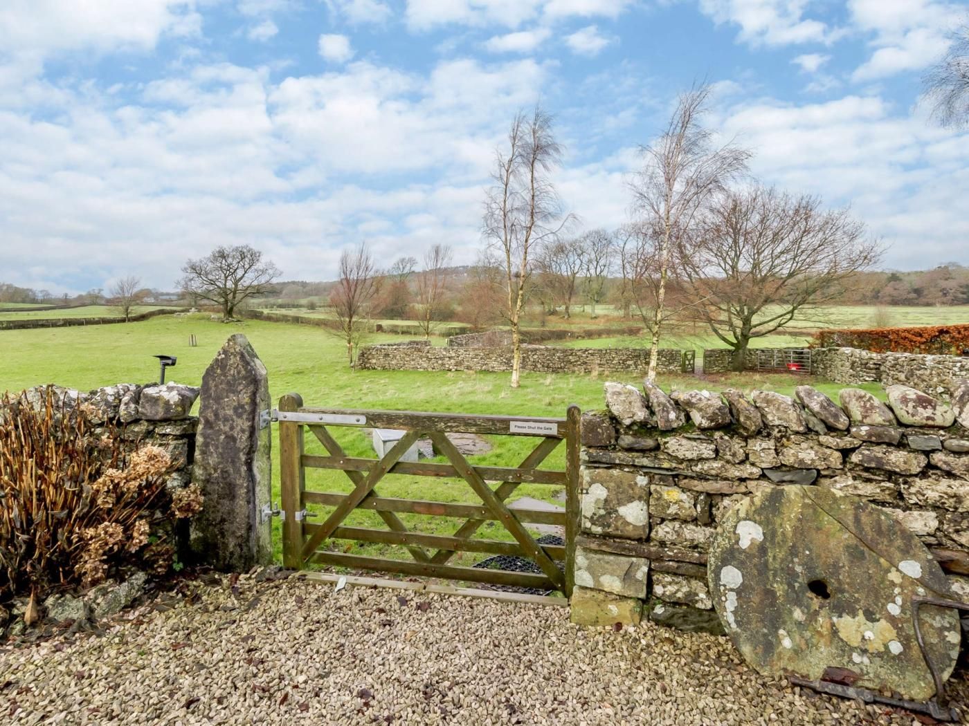 A rural landscape with a stone wall, a wooden gate, and a clear sky.
