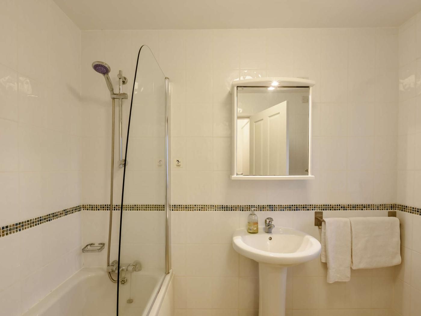 A bathroom with a glass-enclosed shower, a sink with a mirror above it, and a towel hanging on the wall.