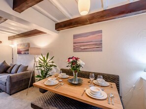 A dining area with a wooden table set for two, a sofa, and a painting on the wall. - 3 Bed in Carnforth (oc-90531) (Yealand Redmayne)