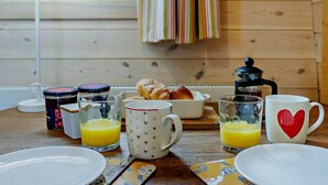 En frukostuppsättning med en kaffebryggare, croissanter och glas för juice, placerat på ett träbord.