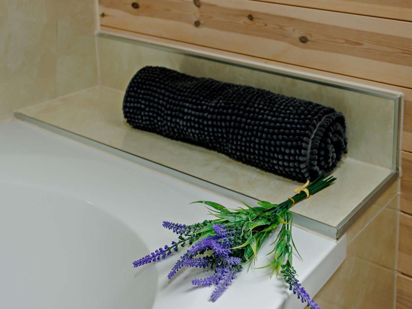 A bathroom with a glass-enclosed bathtub, a rolled-up black towel, and a bunch of lavender flowers.