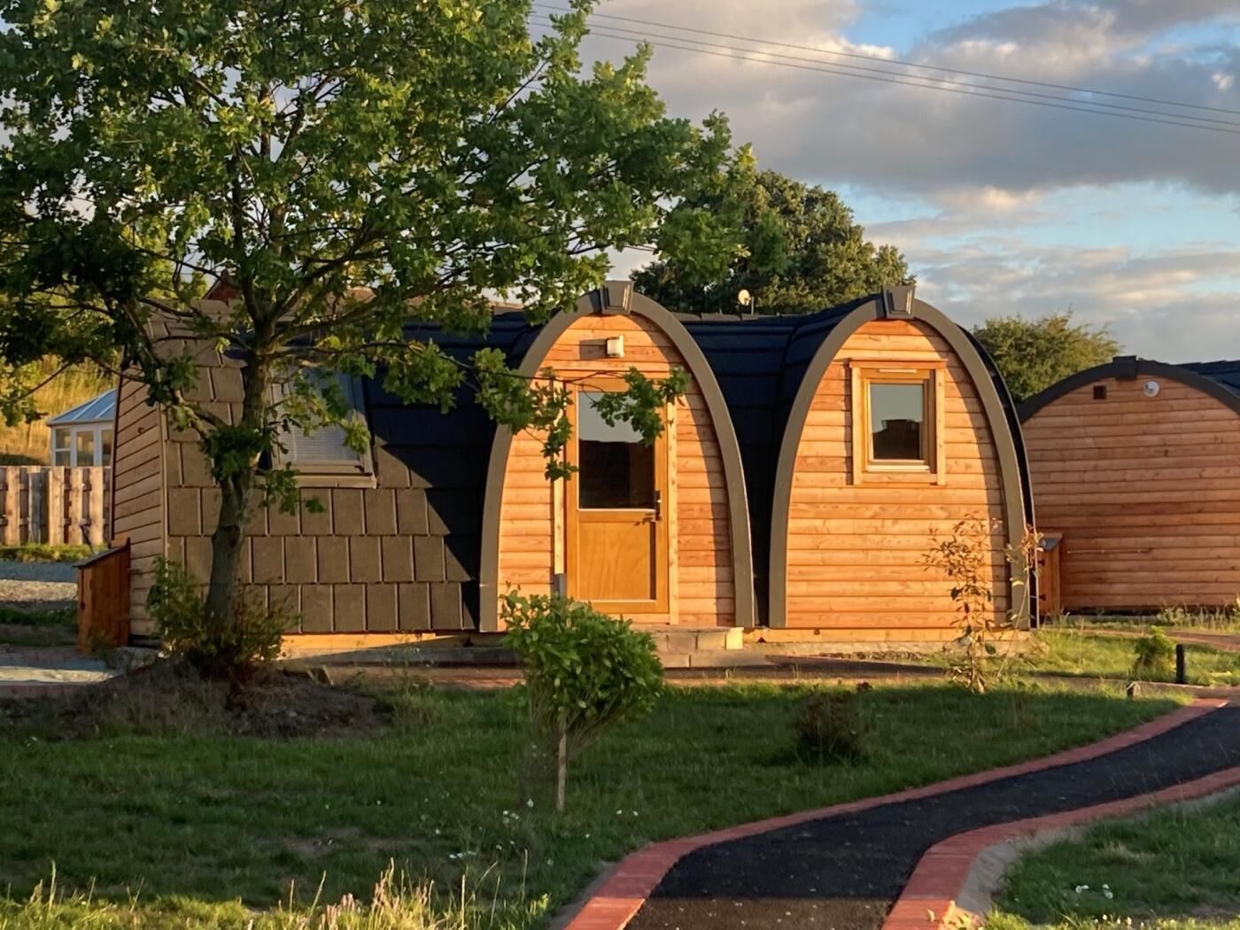 A row of wooden cabins with arched roofs, a paved pathway, and a tree in the foreground.