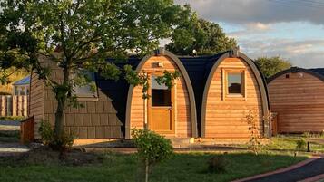 A row of wooden cabins with arched roofs, a paved pathway, and a tree in the foreground.