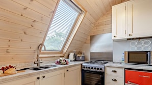 A compact kitchen with a skylight, a gas stove, a microwave, and a red refrigerator.