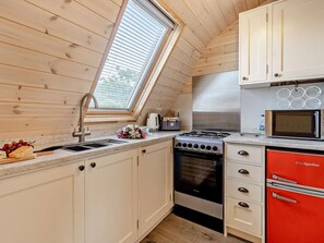 A compact kitchen with a skylight, a gas stove, a microwave, and a red refrigerator.