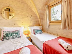Une chambre confortable de style cabane, avec deux lits, un miroir, une fenêtre avec des rideaux et une lampe.
