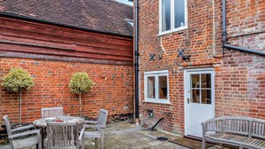 A brick building with a white door and windows, a round table with chairs, and two potted plants. - 3 Bed in Stockbridge (oc-94143) (Broughton)