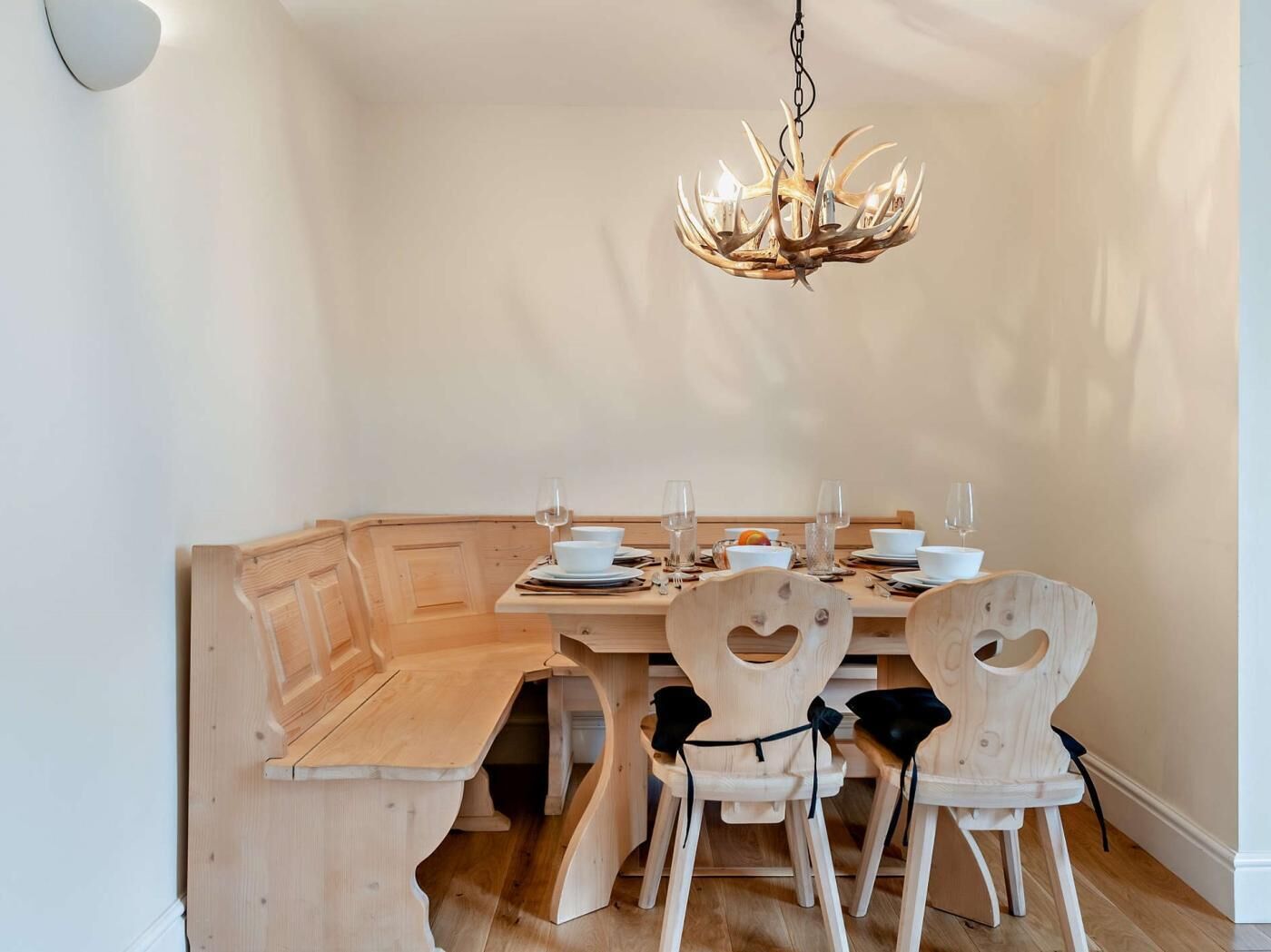 Un coin repas avec un banc en bois servant de siège, un lustre et une table dressée pour quatre personnes.