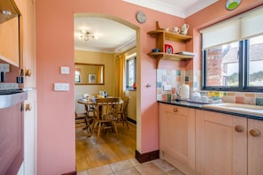 A kitchen with wooden cabinets, a dining table with chairs, and a window with a view. - 2 Bed in Dorchester (oc-dc018) (Winfrith Newburgh)