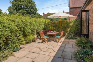 A patio with a table and chairs, surrounded by dense foliage and a brick wall. - 2 Bed in Dorchester (oc-dc018) (Winfrith Newburgh)