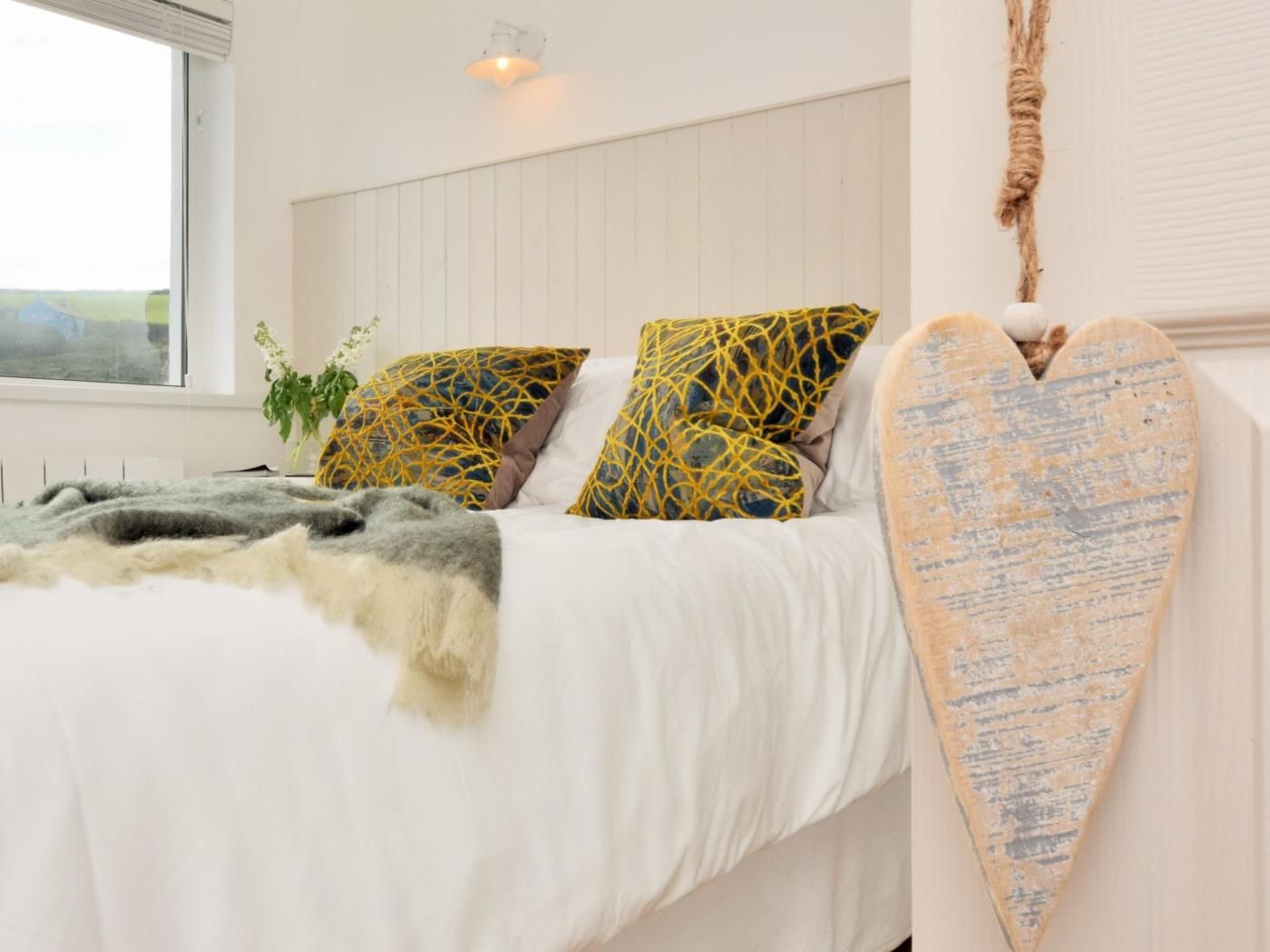 A bedroom with a bed, pillows, a heart-shaped wall decoration, and a window.
