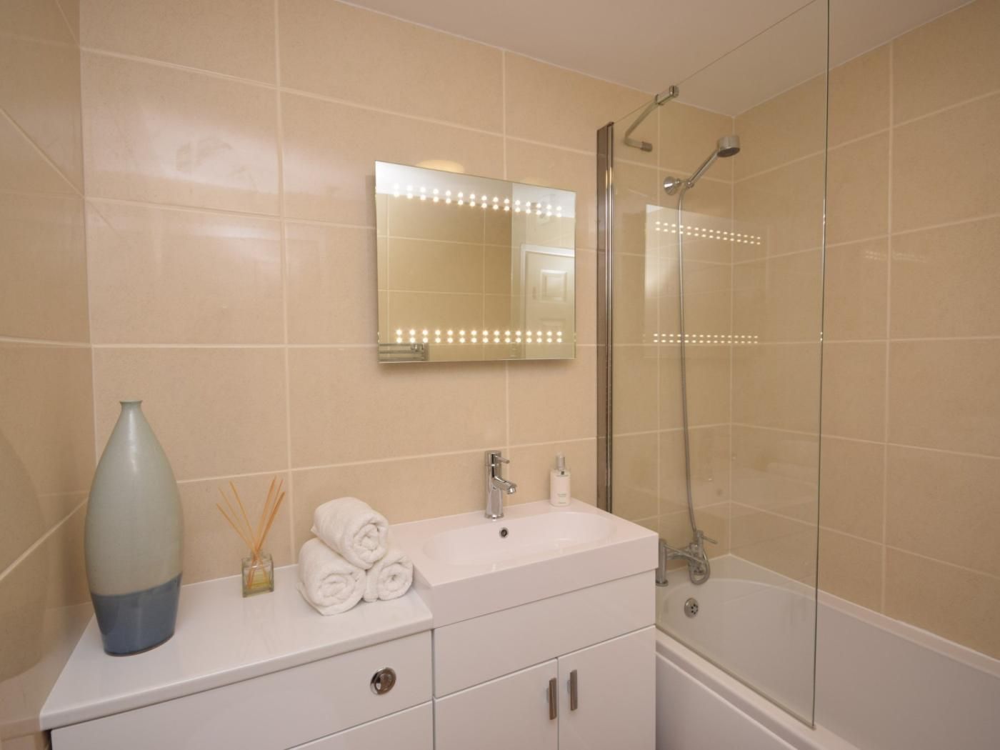 Une salle de bain comprenant un meuble-lavabo, un miroir avec éclairage, une douche et une baignoire.