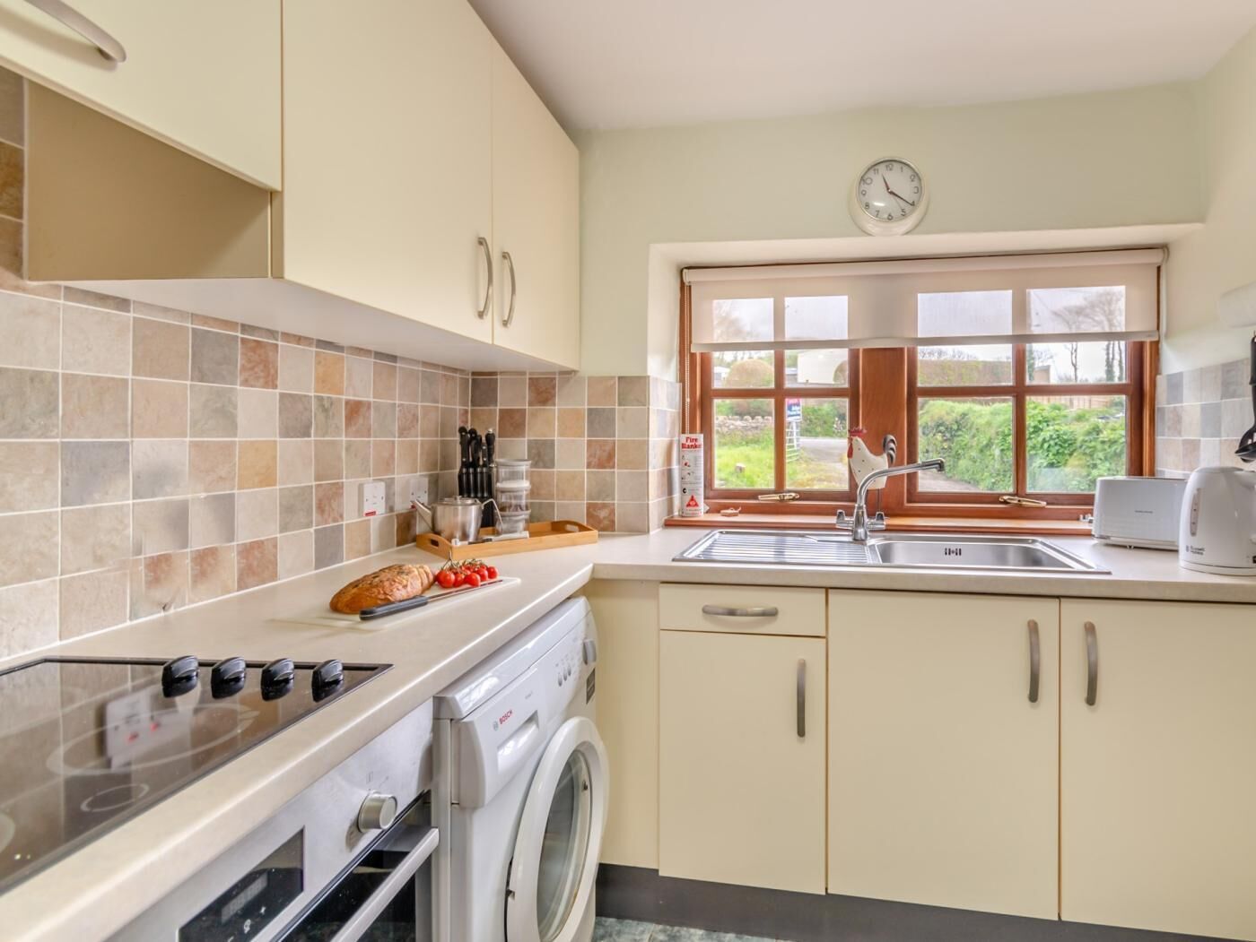 A kitchen with a washing machine, a stove, a sink, and a window with a view of greenery.