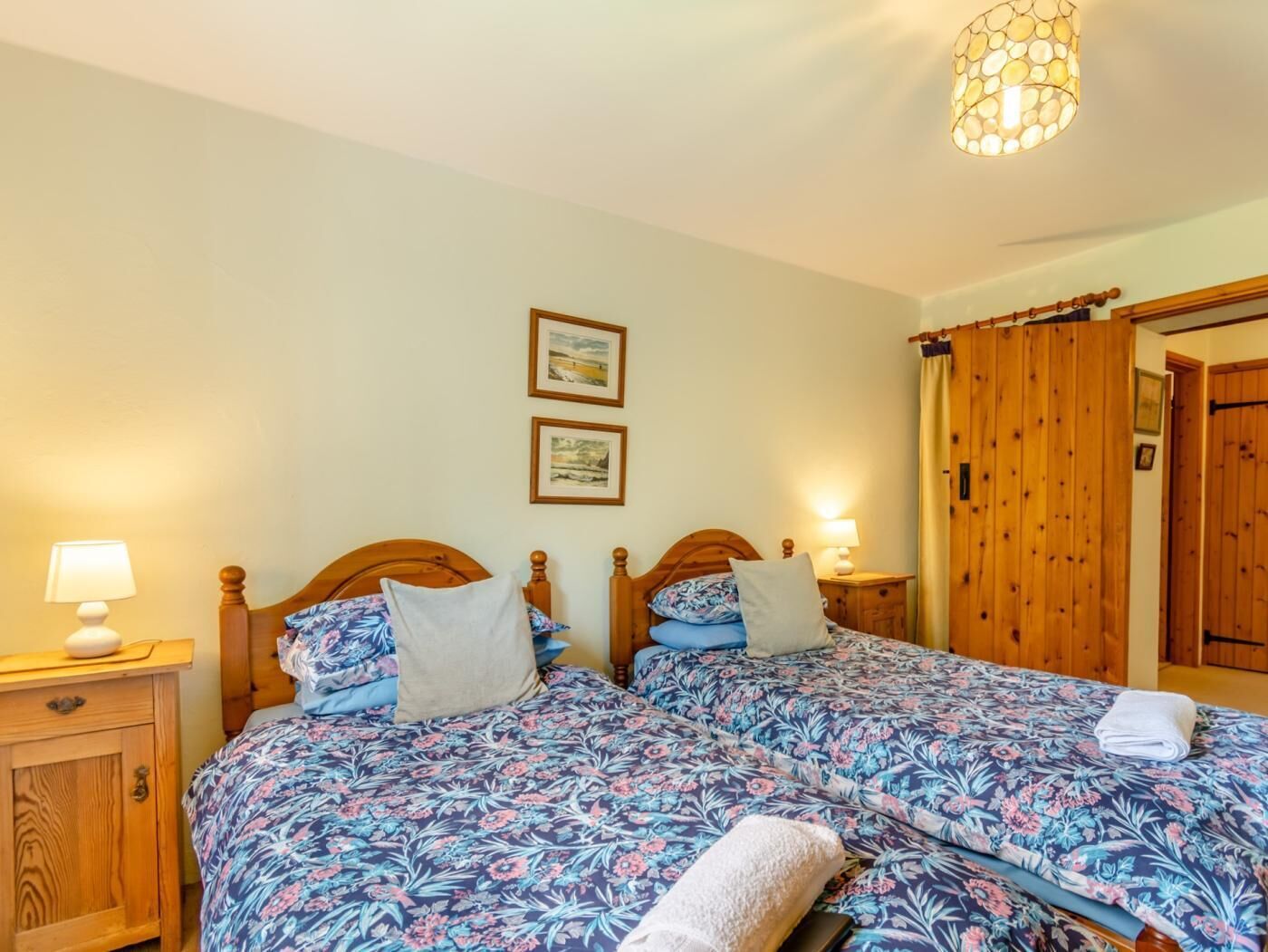 Uma cama de casal com roupa de cama florida, cabeceiras de madeira, luminárias de cabeceira e duas molduras na parede.
