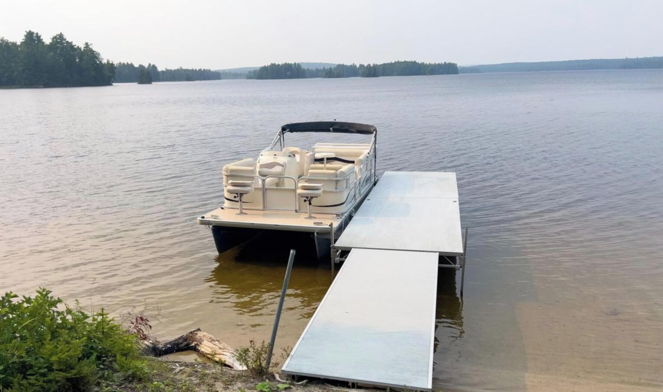 A boat docked at a calm lake with a flat deck and seating area.