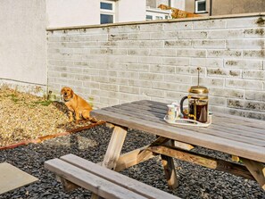 A wooden picnic table with a coffee pot and a cup, a dog sitting on the ground, and a brick wall in the background. - 2 Bed in Millom (oc-93608) (Millom Without)