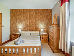 Un dormitorio con cabecera de madera, una cama con ropa de cama a rayas, dos mesitas de noche con lámparas, un aparador de madera y una ventana con cortinas.