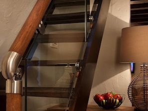 A staircase with a glass railing, a wooden handrail, a wall-mounted lamp, and a fruit bowl on the landing. - 1 Bed in Grange Over Sands (oc-lcc32) (Lindale)