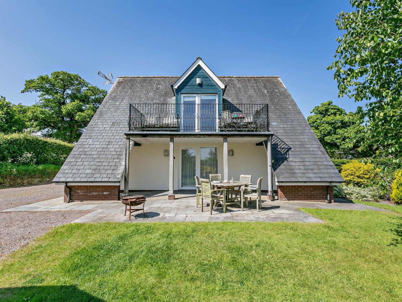 Een tweelaags huis met een balkon, een voordeur en een patio met buitenmeubilair.