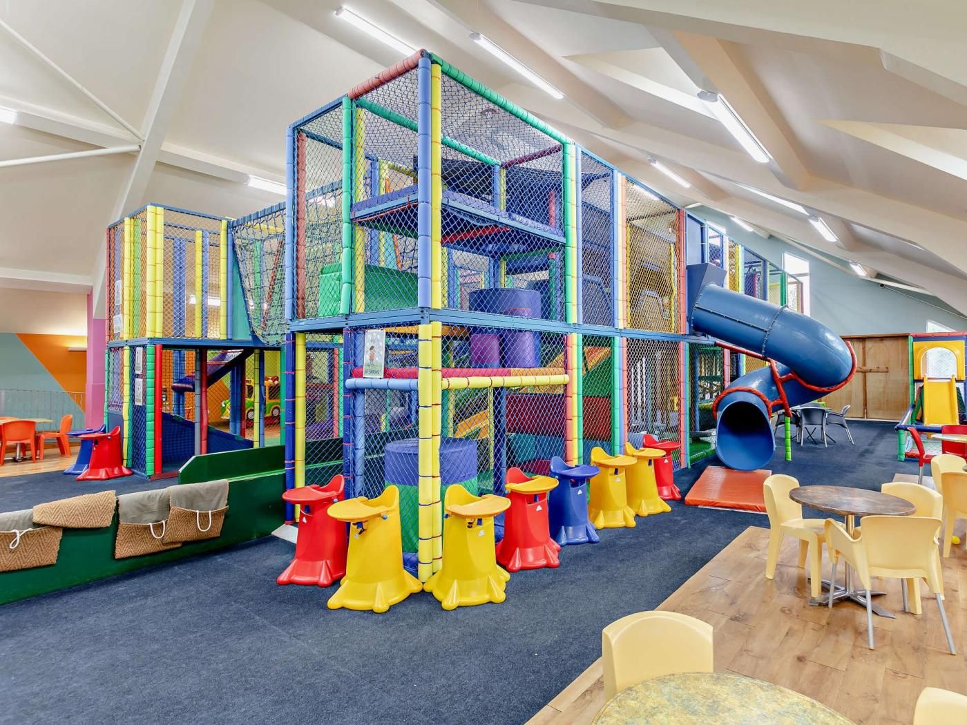 A play area with a multi-level climbing structure, a slide, and seating areas.