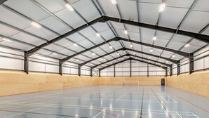 Eine Sporthalle mit hoher Decke, eingezeichneten Sportfeldern und einem Netz in der Mitte.