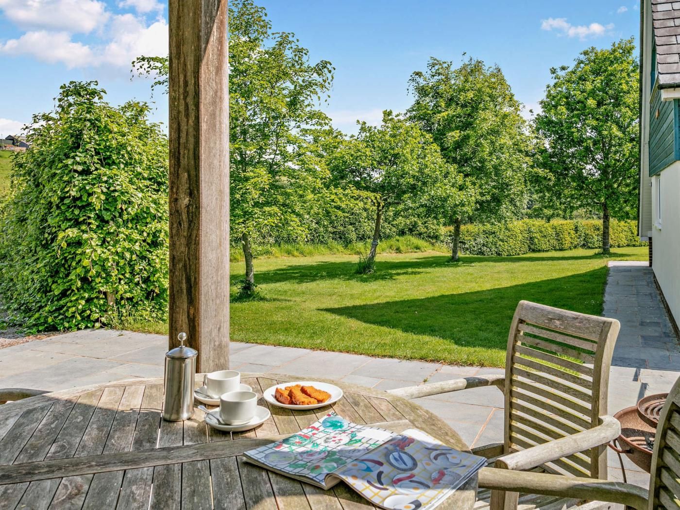 An outdoor patio with a wooden table, chairs, and a metal kettle.