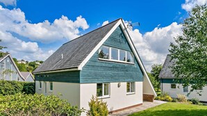 Ein zweistöckiges Haus mit geneigtem Dach, einem sichtbaren Schornstein und einem gepflegten Rasen.