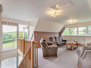 A spacious living room with a high ceiling, a wooden staircase, and large windows offering a view of the countryside. - 3 Bed in Crediton (oc-waie4) (Zeal Monachorum)