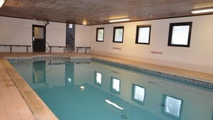 Una piscina interior con paredes de azulejos, techo de madera y vista despejada a la zona de la piscina.