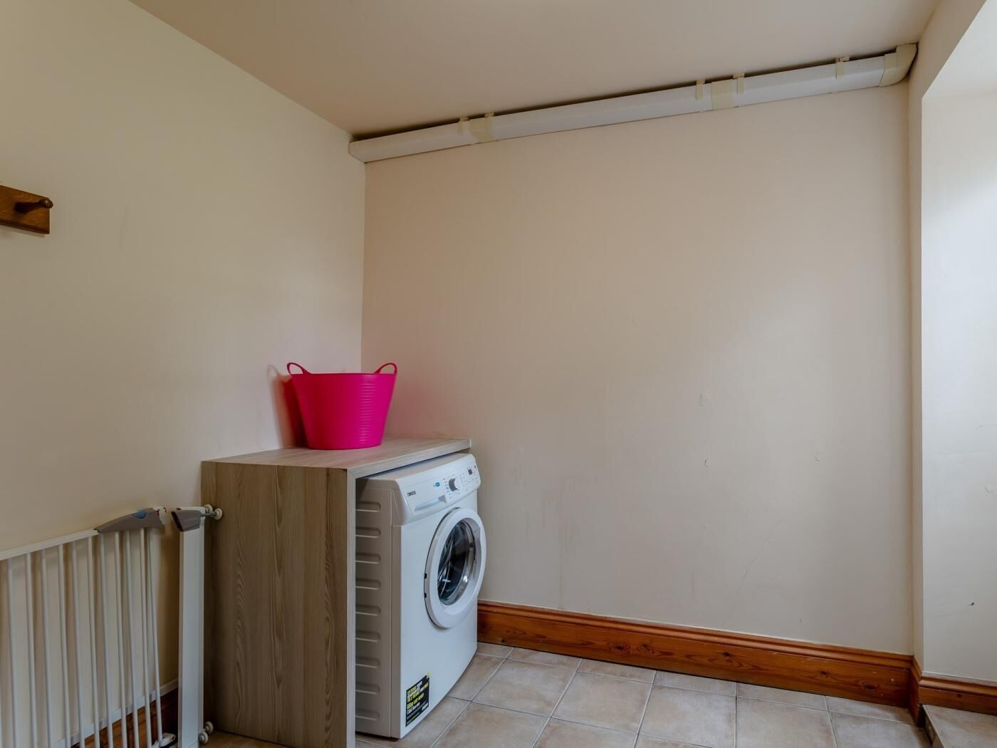 Une buanderie équipée d’un lave-linge, d’une armoire en bois, d’un seau rose et d’un radiateur.