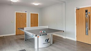 Una mesa de ping pong en una habitación con dos puertas de madera, una lámpara en el techo y suelo de madera.