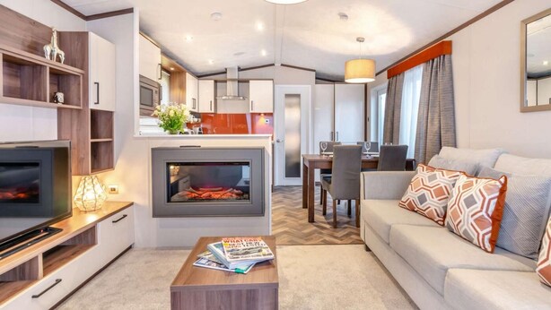 Ein modernes Wohnzimmer mit Kamin, einer Couch, einem Couchtisch mit Zeitschriften, einem Fernseher und einem Essbereich mit Tisch und Stühlen.