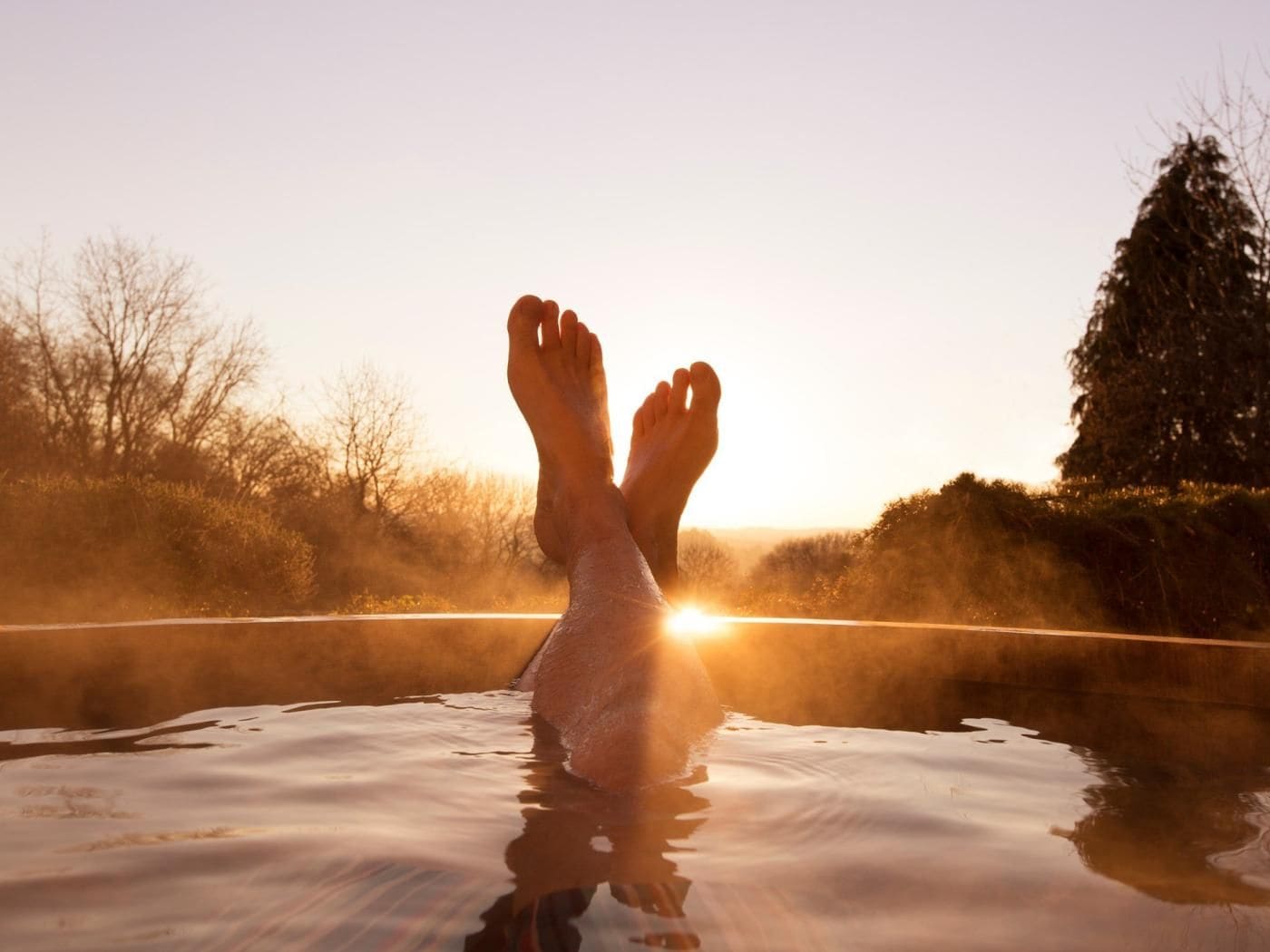 Iemand ontspant in een jacuzzi met een zonsondergang op de achtergrond.