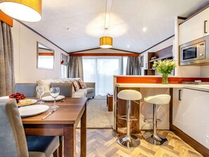 A modern kitchen with a microwave, a dining area with a table and chairs, and a sofa in the background. - 2 Bed in St. Andrews (oc-90763) (St Andrews)