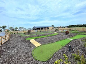 En minigolfbane med flere huller, et træhegn og en bygning i baggrunden.