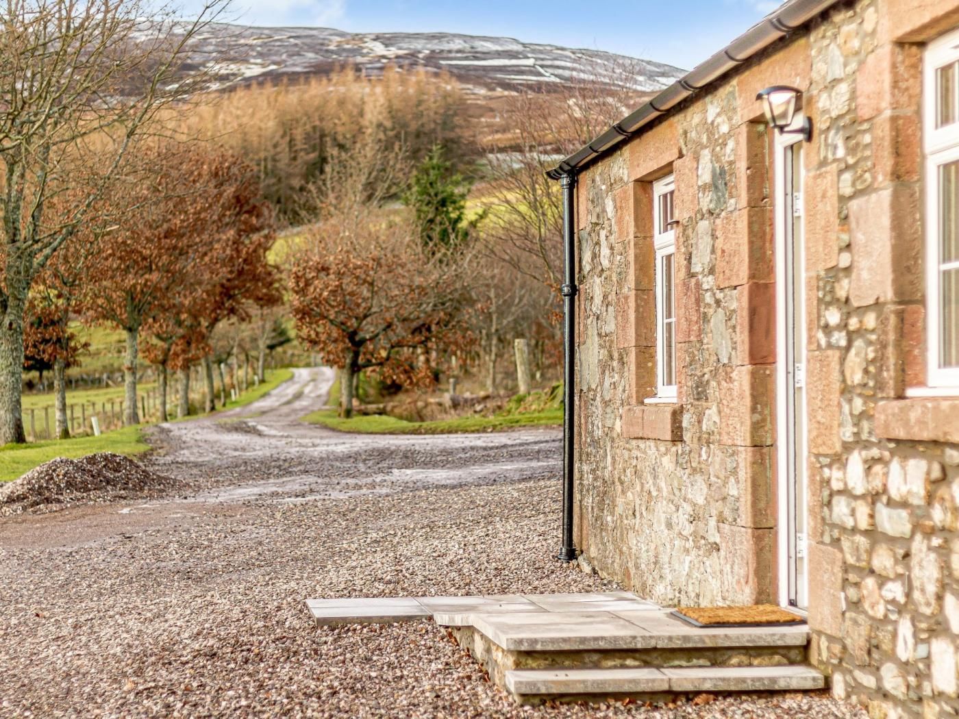 A stone building with a gravel driveway leading to a wooden door.