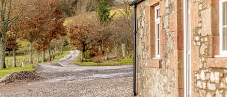 A stone building with a gravel driveway leading to a wooden door.