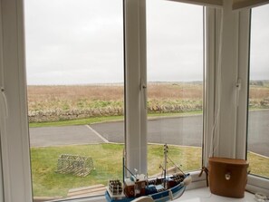 Ein Zimmer mit einem großen Fenster und Blick auf eine ländliche Landschaft, einem kleinen Modellschiff und einer braunen Leder Tasche auf dem Fensterbrett.
