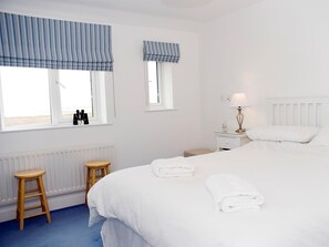 Ein Schlafzimmer mit einem Bett, zwei Fenstern mit blauen Vorhängen, einem Nachttisch mit Lampe und einer Heizung.