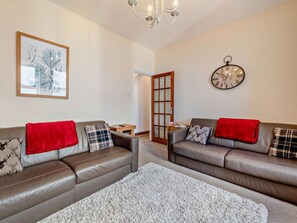 Ein Wohnzimmer mit zwei Ledersofas, einem Teppich, einer Uhr und einem gerahmten Bild an der Wand.