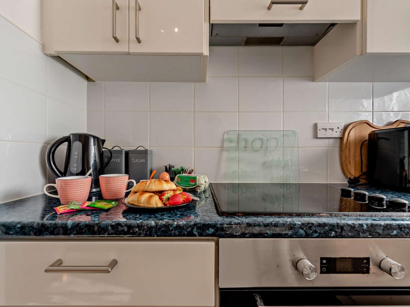 A kitchen with a black countertop, a coffee maker, sugar and coffee containers, a glass display case, and a microwave.