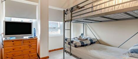A compact room with bunk beds, a television, and a wooden dresser.