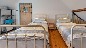 A bedroom with two beds, a wooden door, and a metal shelf unit. - 2 Bed in Haverfordwest (oc-93577) (Marloes)