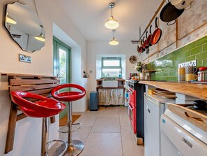 Una cocina con un taburete rojo, un lavavajillas blanco y un salpicadero de azulejos verdes.
