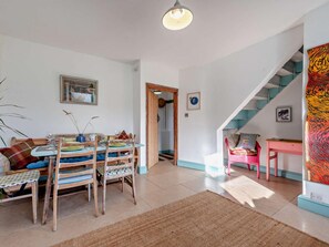 Un comedor con mesa y sillas, una escalera y una puerta que da a otra habitación.