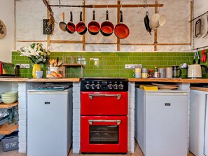 A kitchen with a red oven, a green tiled backsplash, and hanging pots. - 2 Bed in Haverfordwest (oc-93577) (Marloes)