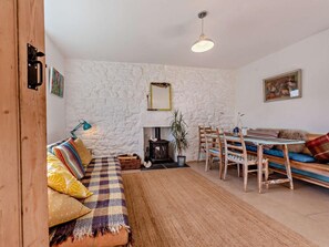 Una sala de estar acogedora con una pared de piedra, un sofá con cojines de colores, una mesa de comedor con sillas y una lámpara colgante.