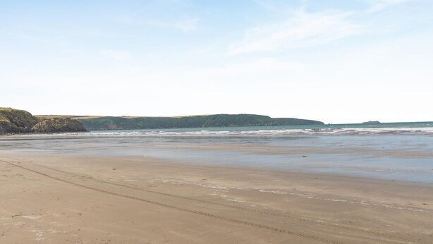 Ein Strand mit sandigem Ufer, Wellen und einer entfernten Hügelkette.